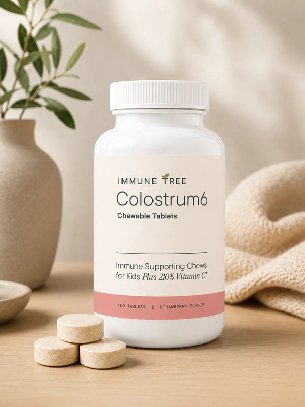 Immune Tree Colostrum6 Strawberry Moo Chews 180 tablet supplement bottle clean product shot on a warm wood surface with a ceramic vase and plant leaves in the background and loose chewable tablets in the foreground, showing the full front label